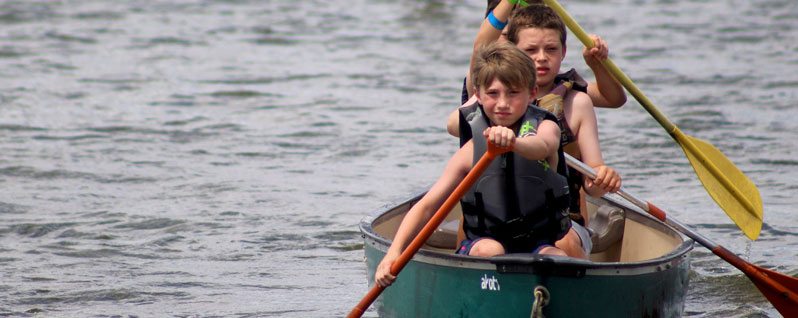 Three boys paddling a canoe on a lake.